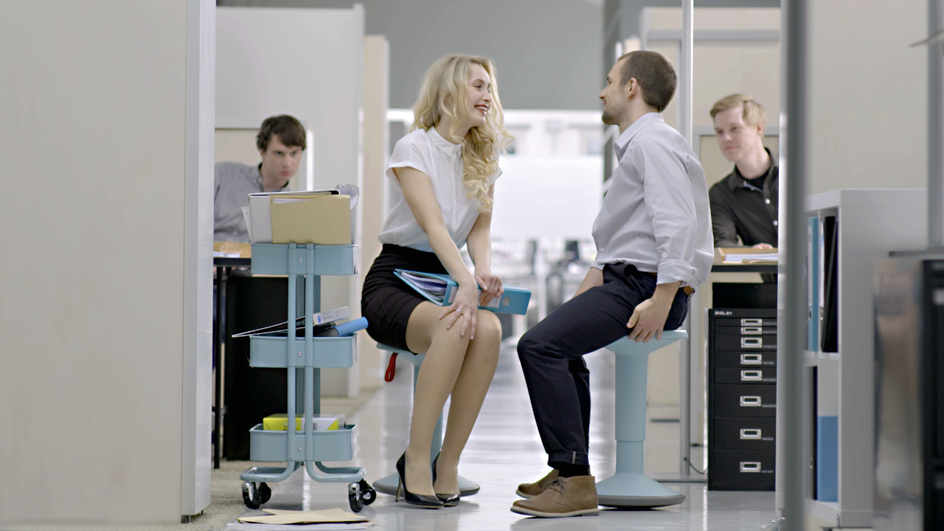 two workers sitting on adjustable stools in office hallway