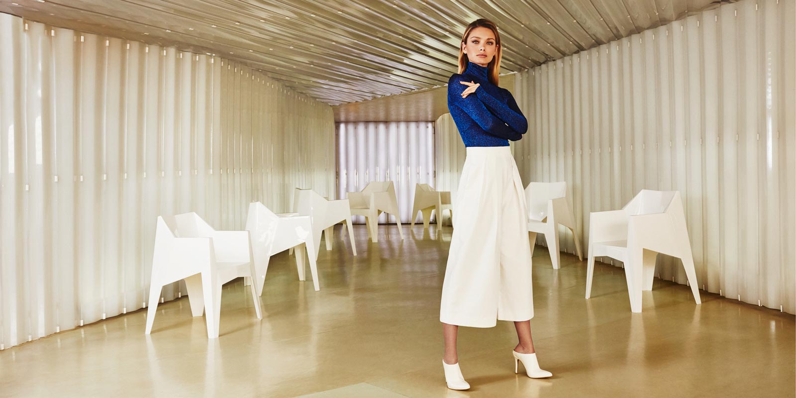 female model standing in front of white poly armchairs