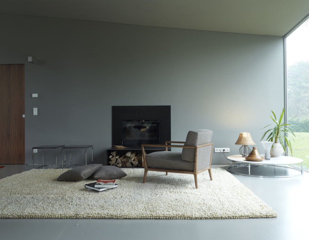 Carlton Armchair for Nube on plush white rug in modern living room with fireplace