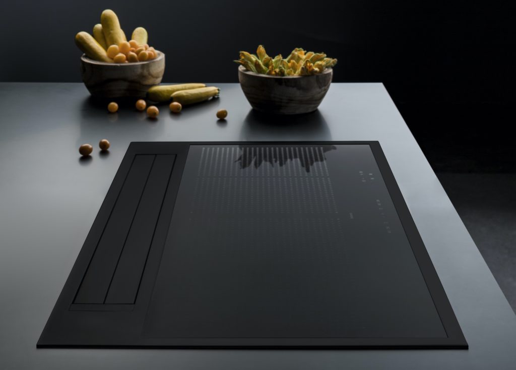 Sintesi total black cooktop view from side on gray countertop with two bowls of food beyond