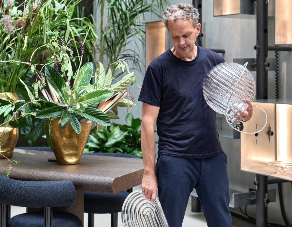 Tom Dixon Press Light Dixon holding uninstalled glass modules in front of table with plants on it 