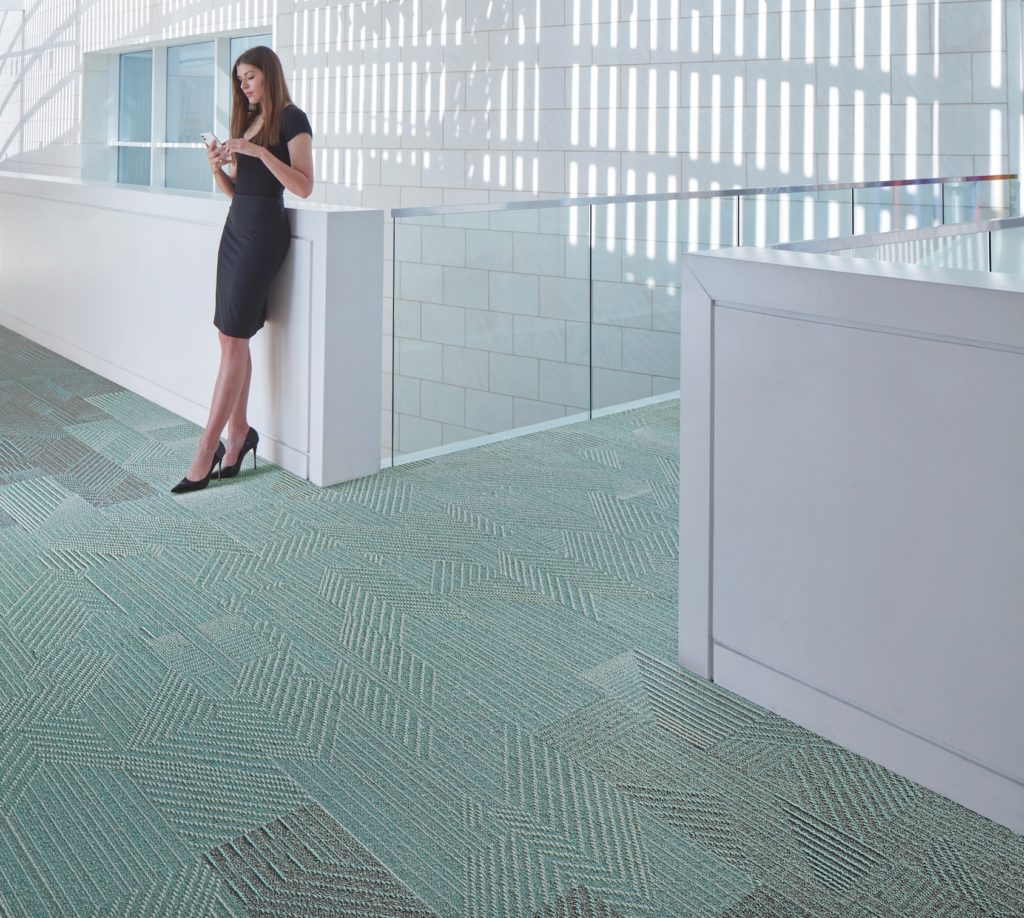 Rising Signs Carpet Tiles Play the Angle straight and angled lines in blue/green and gray with in atrium with woman leaning against half wall