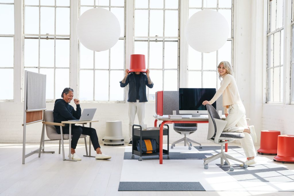 Teknion Routes chairs, desks, mobile stool in primary colors in sunny office with happy people