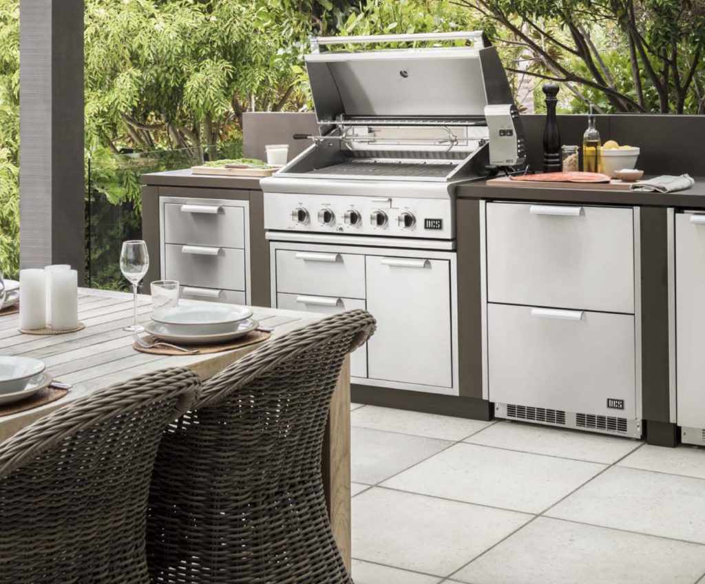 Series 9 DCS grill in outdoor kitchen with food and cooking items and partial view of outdoor table