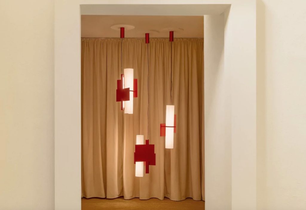 Three Fold chandeliers in red hanging in front of tan-colored curtain