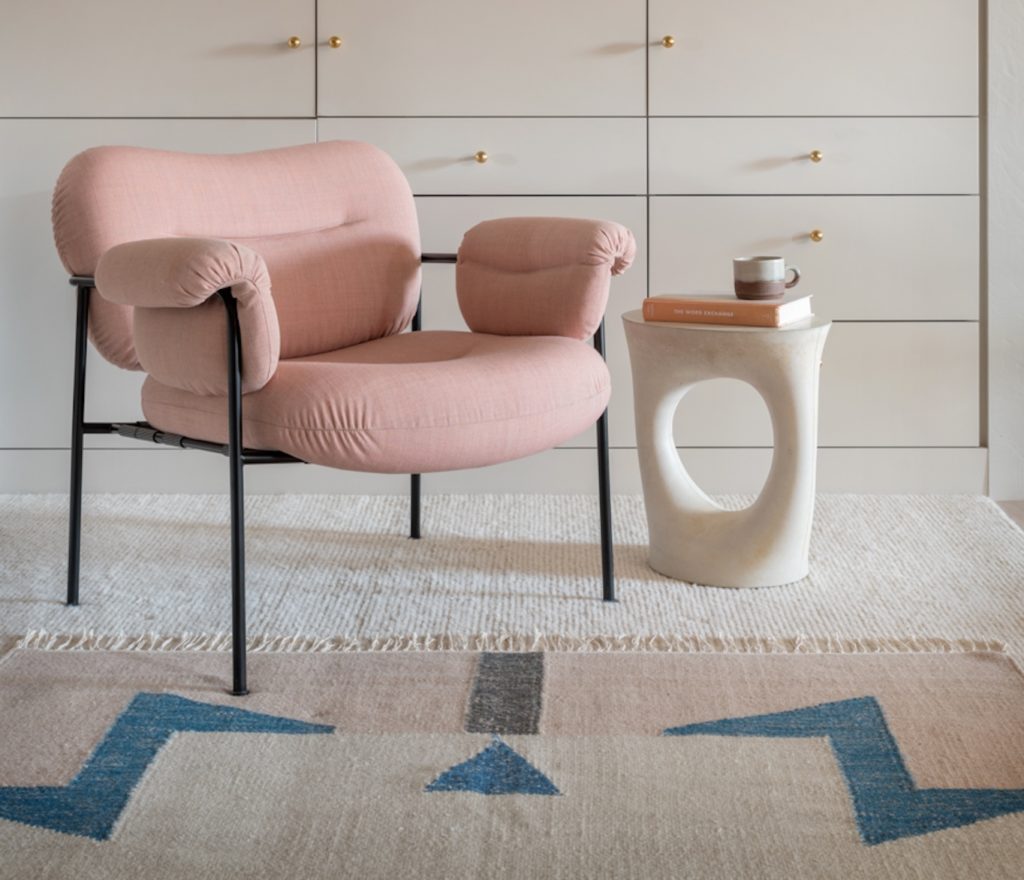 Small table with large hole in the middle next to comfy pink chair on white rug.