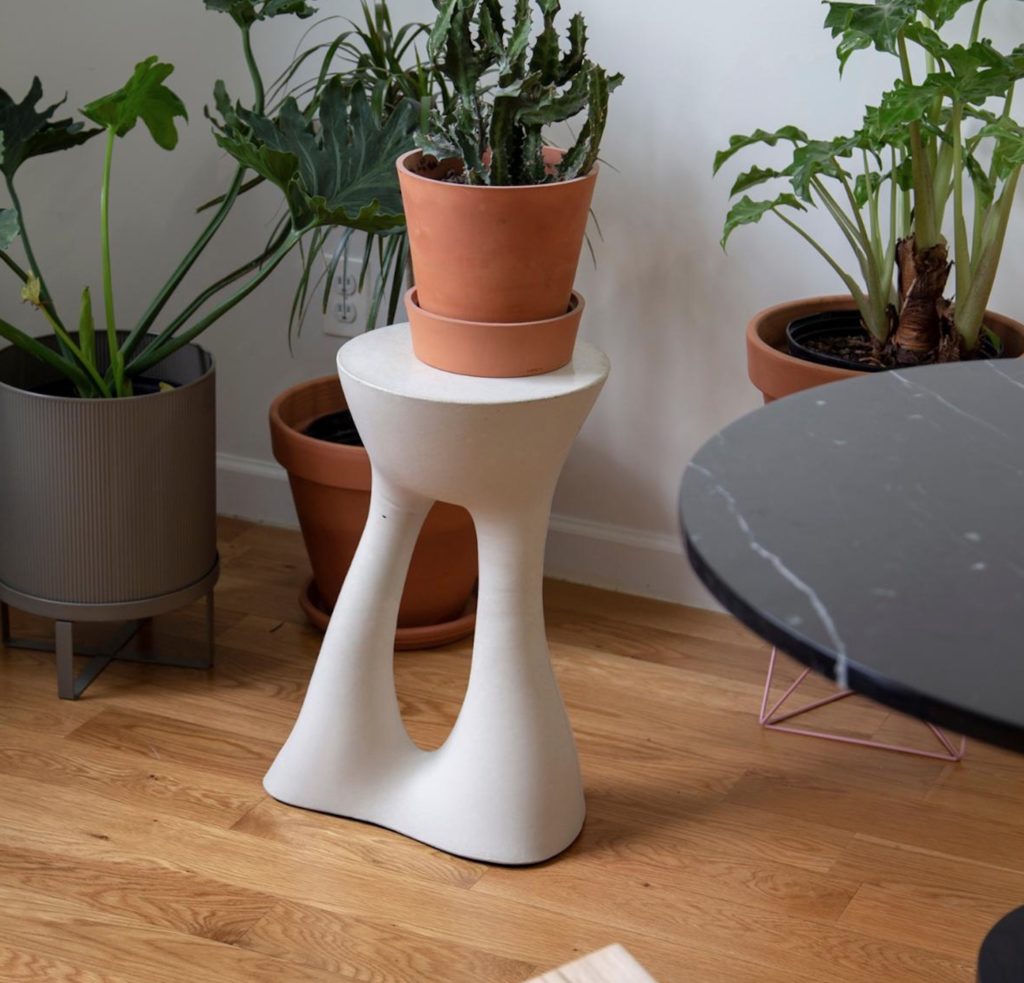 Kreten table in white with a plant on top and several plants around