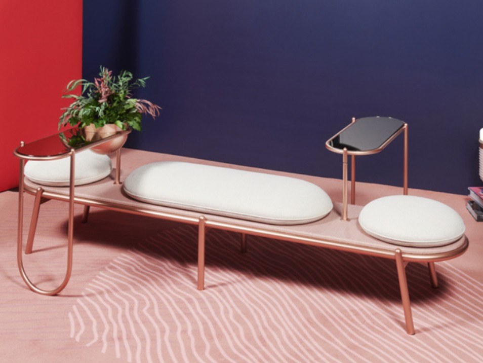 Bench with copper-colored frame and white pillows against a dark blue wall on coral-colored carpet