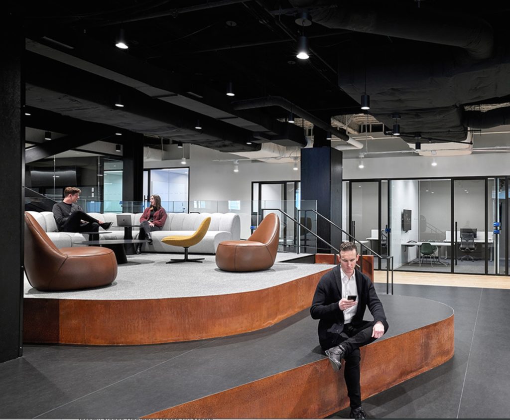 Open space in consultancy firm with gray floor and carpet and comfy modular couch surrounded by glass-walled offices and other spaces