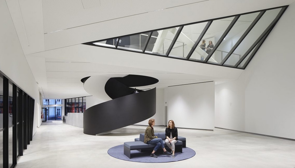 two visitors inside art museum sitting beneath circular staircase and skylight