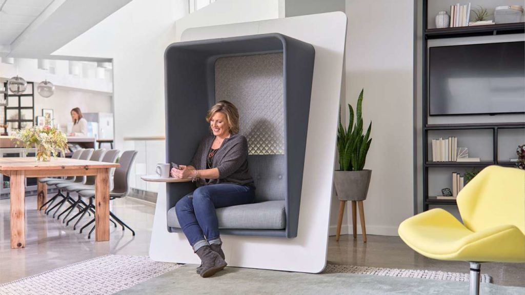 woman sitting in single-seat freestanding upholstered pod with tablet arm
