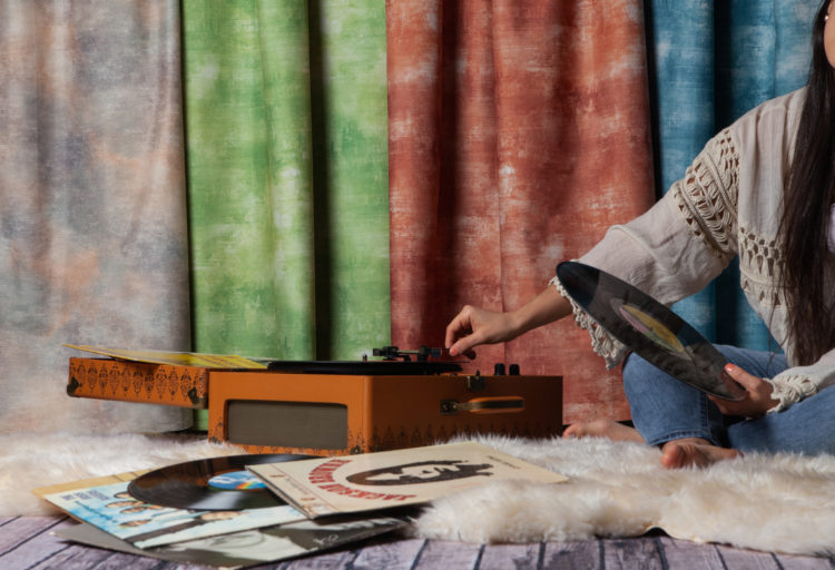 woman playing record player with acid wash draperies behind her