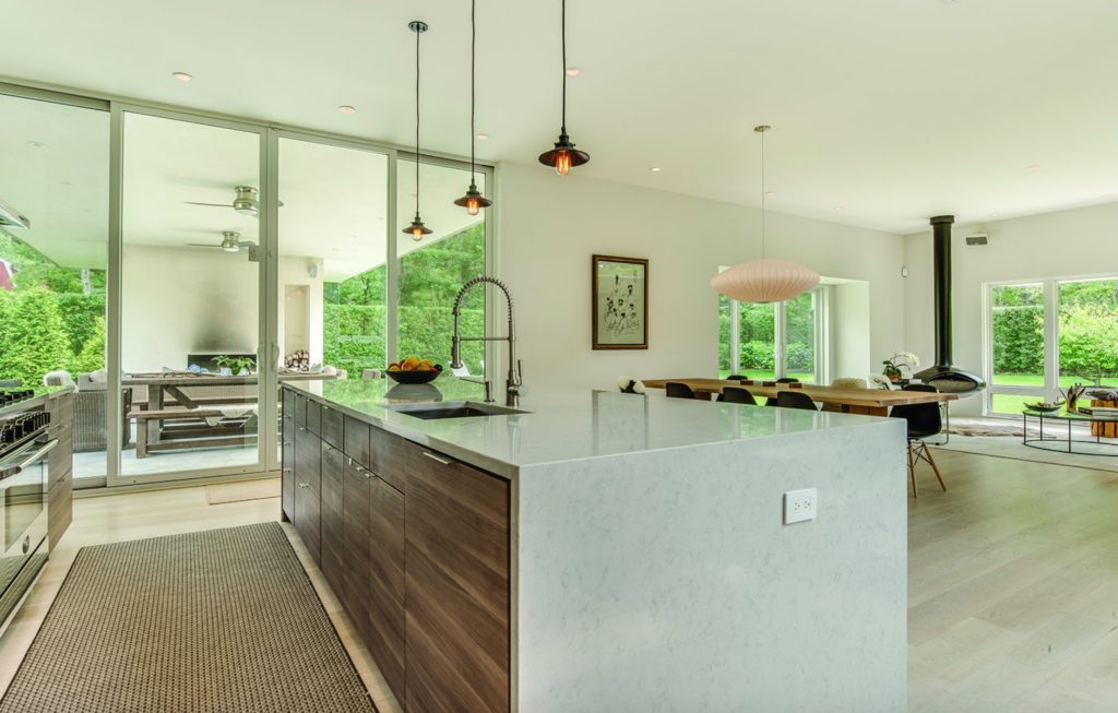 Modern Net Zero Hamptons' home interior image of kitchen with large center island, dining table, and view of back patio