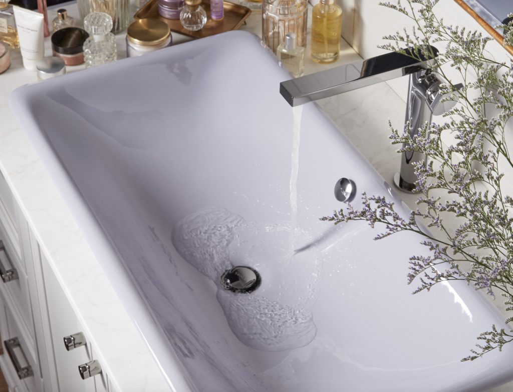 Lavender sink in bathroom view from above with water running and perfume bottles visible