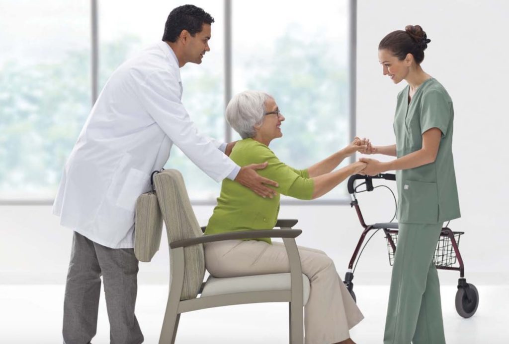 Primacare Seating split back patient chair with gray back and light gray seat elderly woman patient being assisted by doctor and nurse
