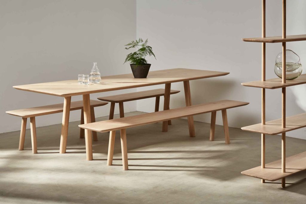 Benchmark Ovo Collection dining table with benches and partial view of shelving in light oak 
