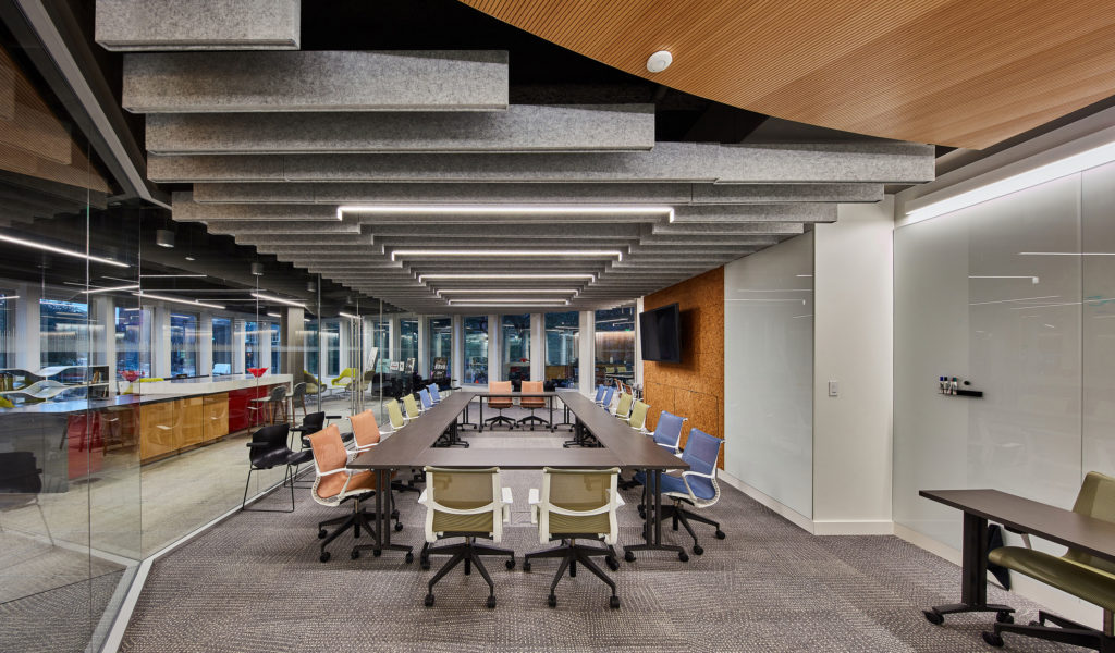 Focal Point Seem 1 Acoustic luminaire different baffle lengths creating coffered ceiling in central workspace with glass partitions