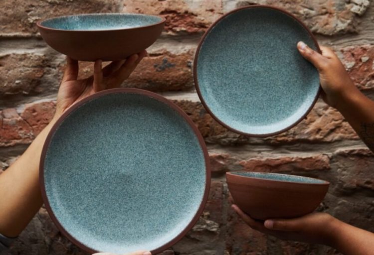 Granbyware plates and bowls with blue/green glaze being held up in front of rock wall