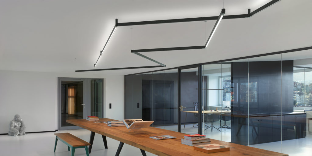 Flos Diversion lighting semi-flush mount, black housing in zig-zag configuration above wooden conference table in workspace with glass walls