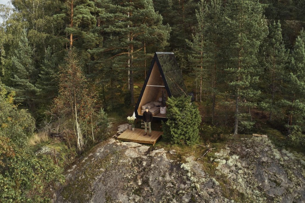 Zero Travel Nolla Cabin view from outside with designer standing on small deck amid rocky cliff and tall pine trees