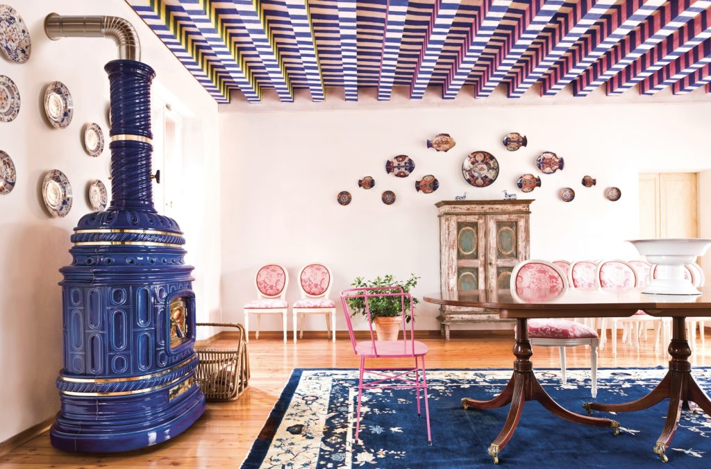 Corsara Stove side view showing stove in ornate room with blue patterned rug, pink an white chairs, wooden table, and drop ceiling with blue/white pattern 
