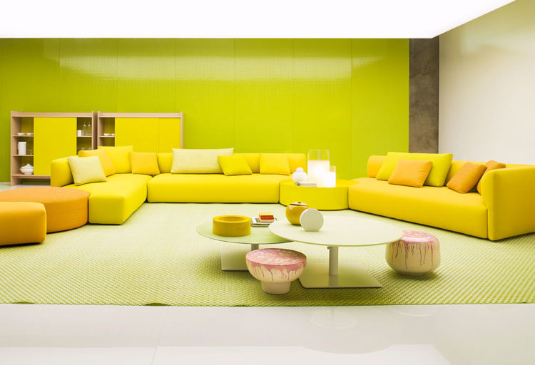 Paola Lenti Walt Seating several sofas in yellow with peach colored poof and additional seating with two separate tables in front of sofa and yellow storage unit behind