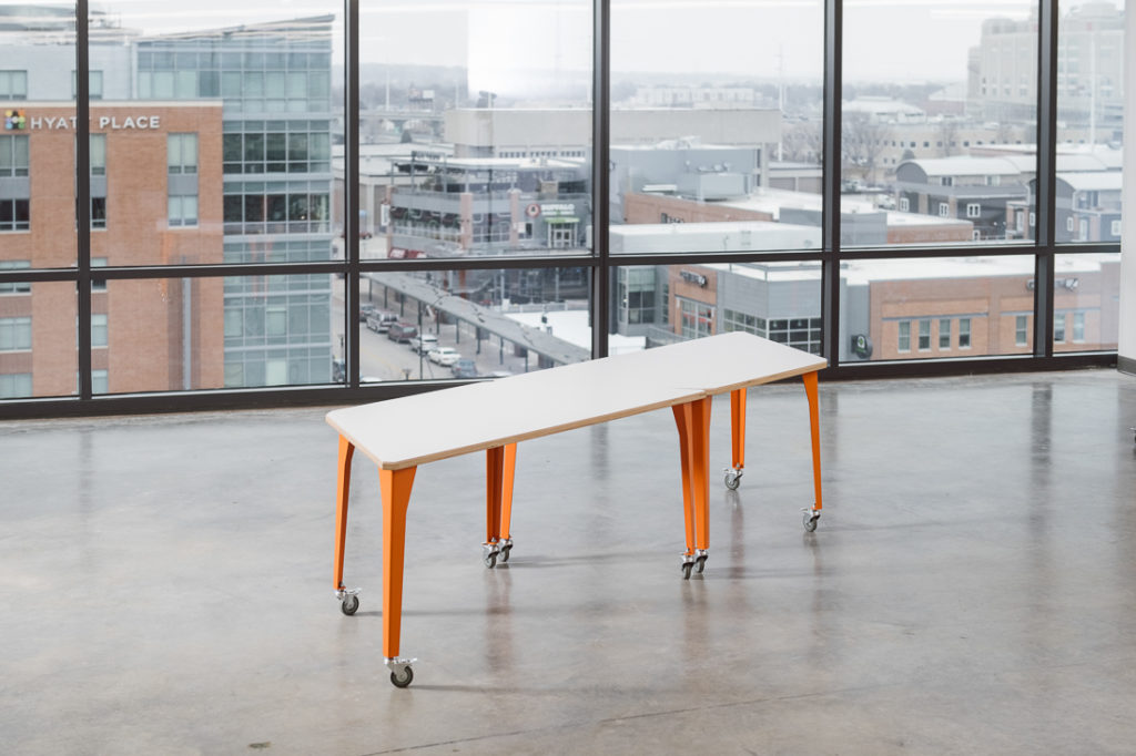Werk Trap Table two tables with orange legs set together to form parallelogram shape in open room with view of city