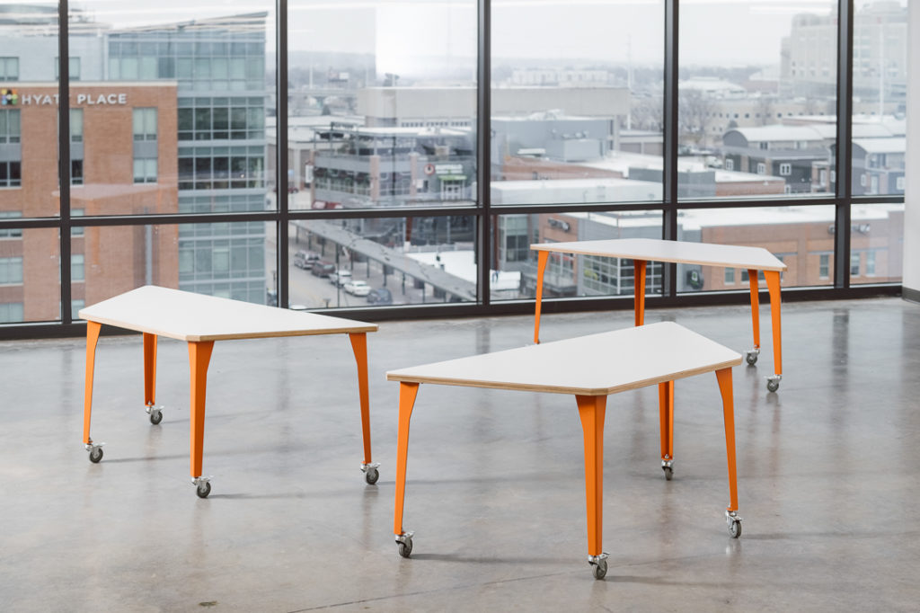 Werk Trap Table three tables with orange legs set apart in open room with view of city