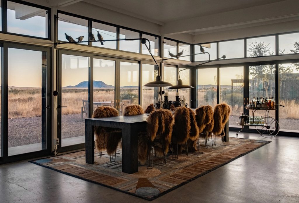 Atlas Collection dining room with rug and large rectangular table with chairs covered in shaggy animal skin and view of desert outdoors