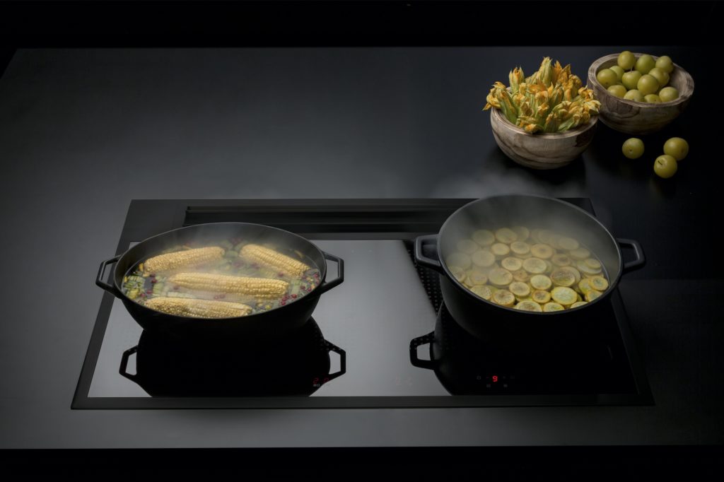 Sintesi total black cooktop front view with two pots of corn and squash cooking and bowls of food in background