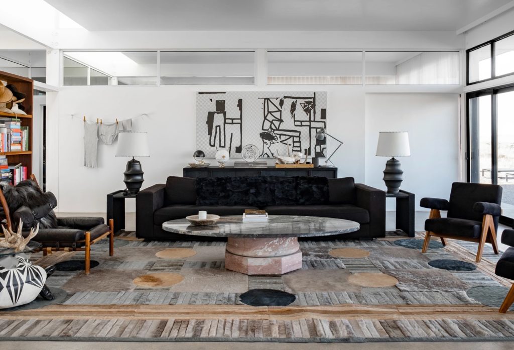 Atlas Collection living room with very large square rug with muted tones in living room with large black sofa, black chairs, and bookcase off to the side