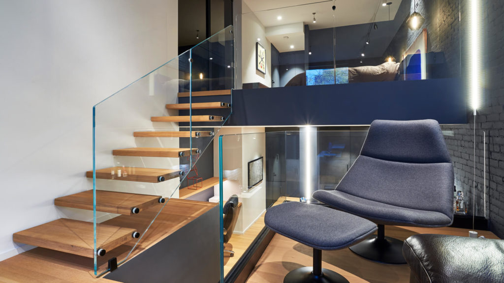 Staircase with broad wooden treads and glass panel style railing in small apartment