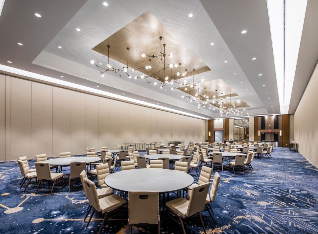 H.E. Williams Lighting chandeliers with thin rods at different angles and spherical lamps in ballroom with many tables and chairs
