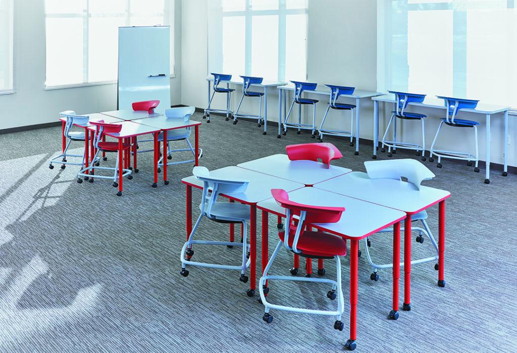 KI Ruckus post-leg desks with white top and red legs two tables in workroom with gray carpet and blue chairs against the window
