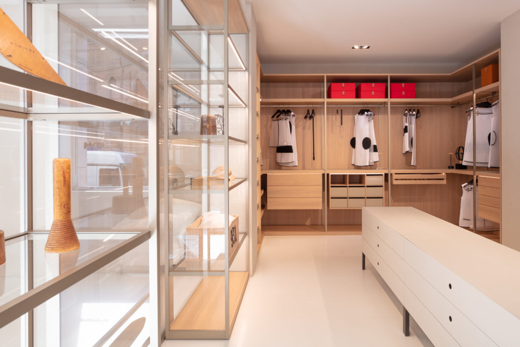 Electric Box wooden storage  with glass shelves and wood paneling and drawers at far end with clothing hanging and red boxes in nook overhead 