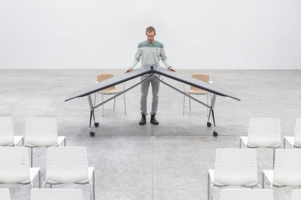 Falcon Ascent Lift Table with man lifting table into mobile mood in large conference hall with chairs