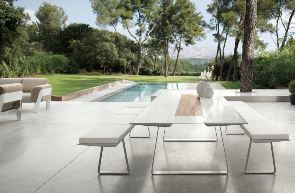 Extrados table outdoors with grassy lawn, large trees, and swimming pool