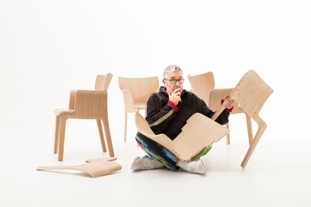 Adela Rex Starck in foreground with three chairs behind and he's holding one that's disassembled into three pieces