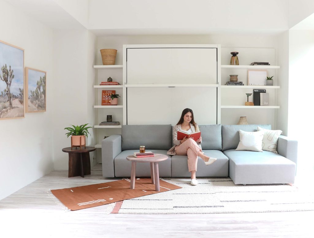 Swing as sofa with white shelves behind in gray upholstery with seated woman reading