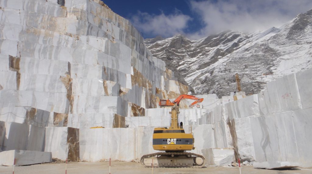 porcelain tile image of a marble quarry in italy with big chunks of the mountain missing and a CAT tractor