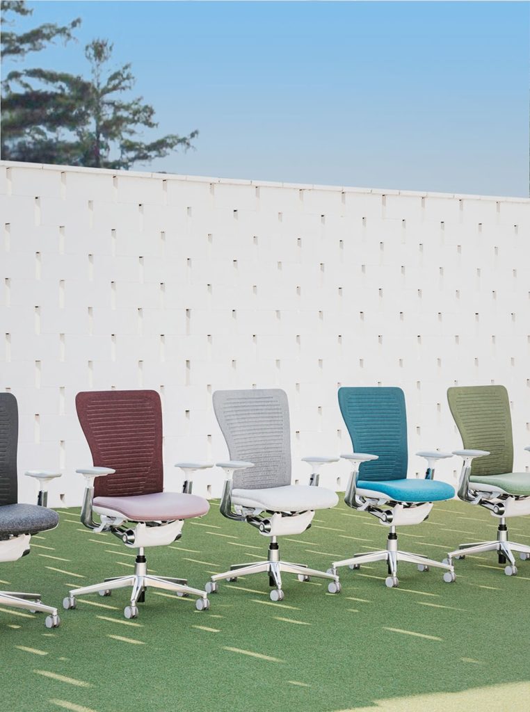 Row of Haworth chairs in different colors outdoors with white wall behind 