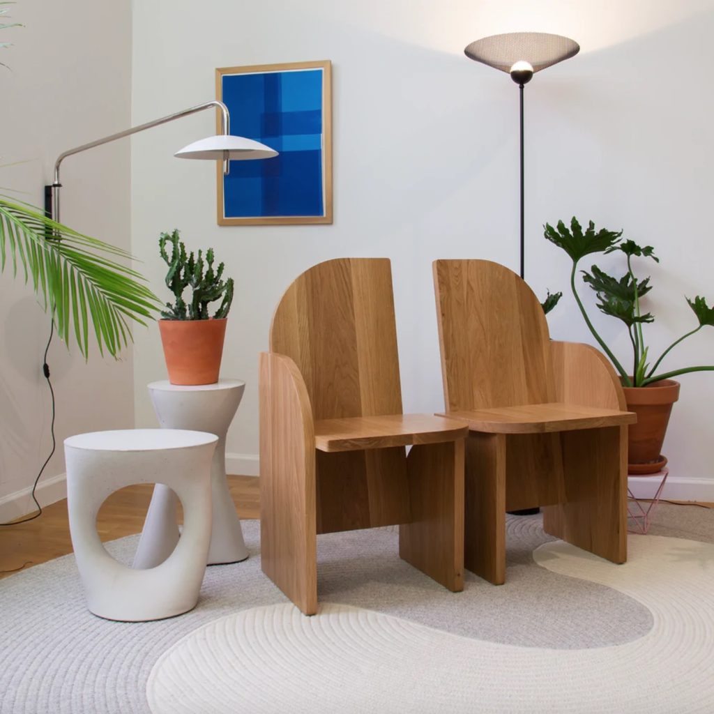 Signal arm sconce in living room with wood chairs and white side table and many plants 