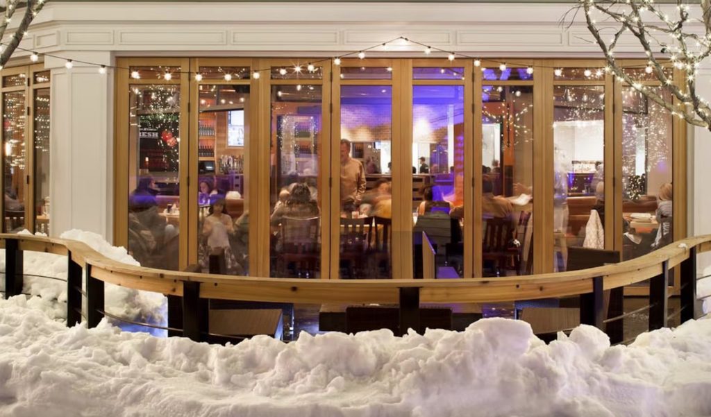 View in winter from outside Park City restaurant in winter with a large glass wall system and a semi-circular deck 
