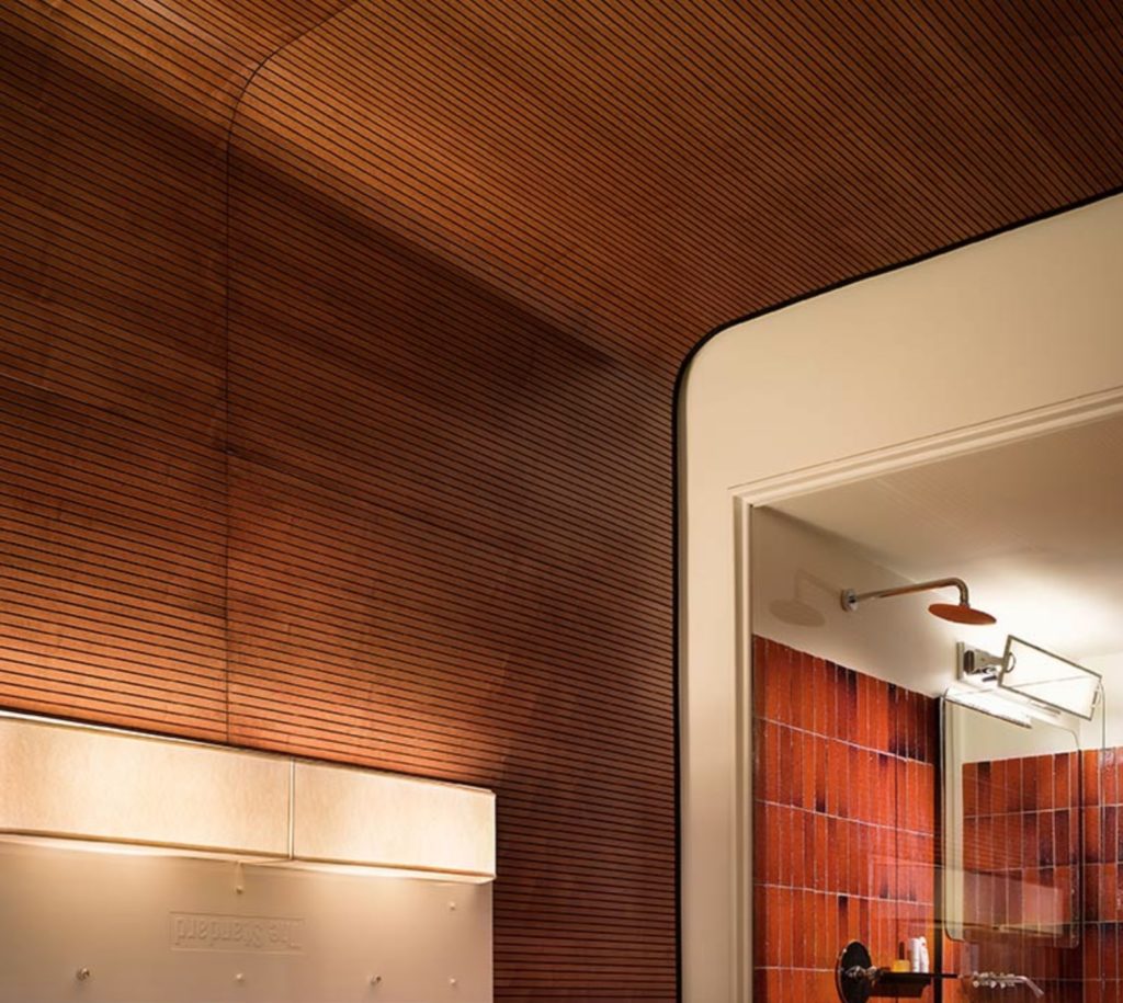 tambour panels in medium-toned wood on wall and ceiling of bedroom with glimpse of bathroom in background