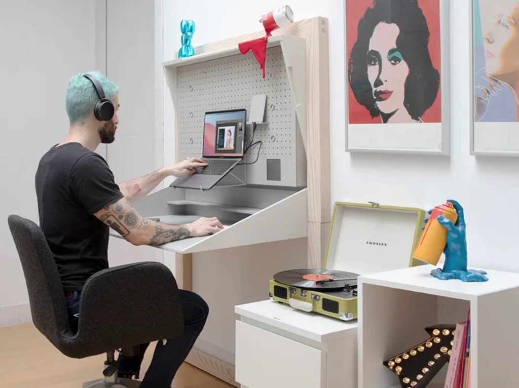 Man with green hair working at Beaktor workstation in home offfice with poppy art and a record player