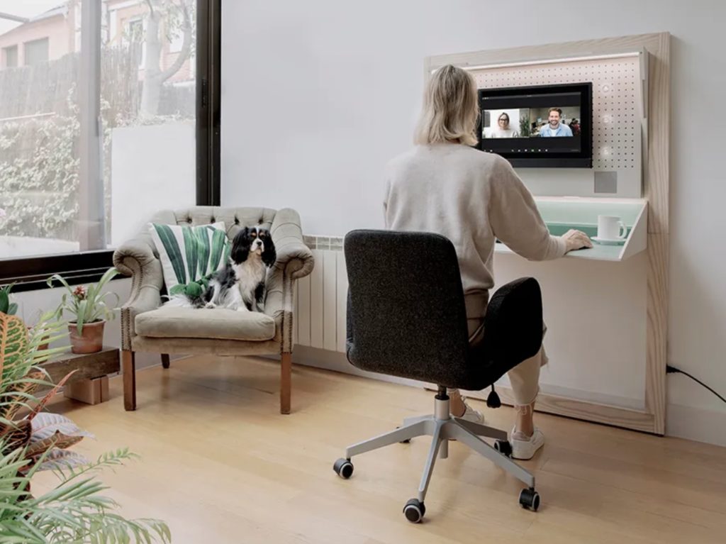 Beaktor desk with woman working and participating in video call and dog on a chair next to her
