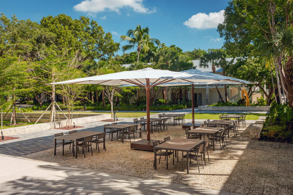 Two large parasols in an outdoor room with tables and chairs set up beneath