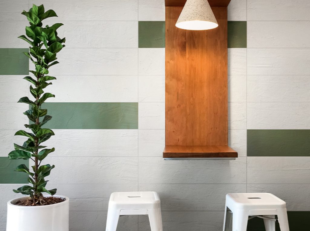 Plaster 2.0 green and white wall tile with plant, stools, and wooden standing desk