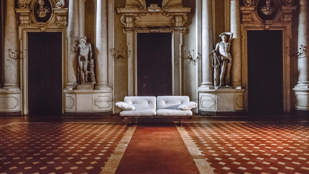 White sofa in large neo-classical gallery setting flanked by David statues