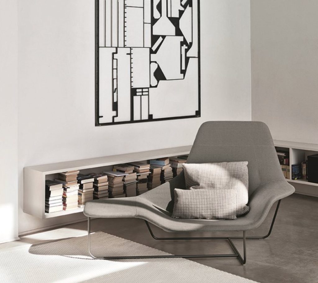 Lounge in gray with gray pillows in white room with books in a low bookcase